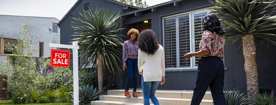 Family in front of home with a for sale sign