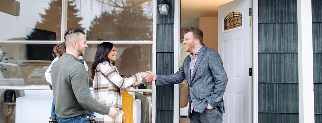 Homebuyers shaking hands with agent in front of a home